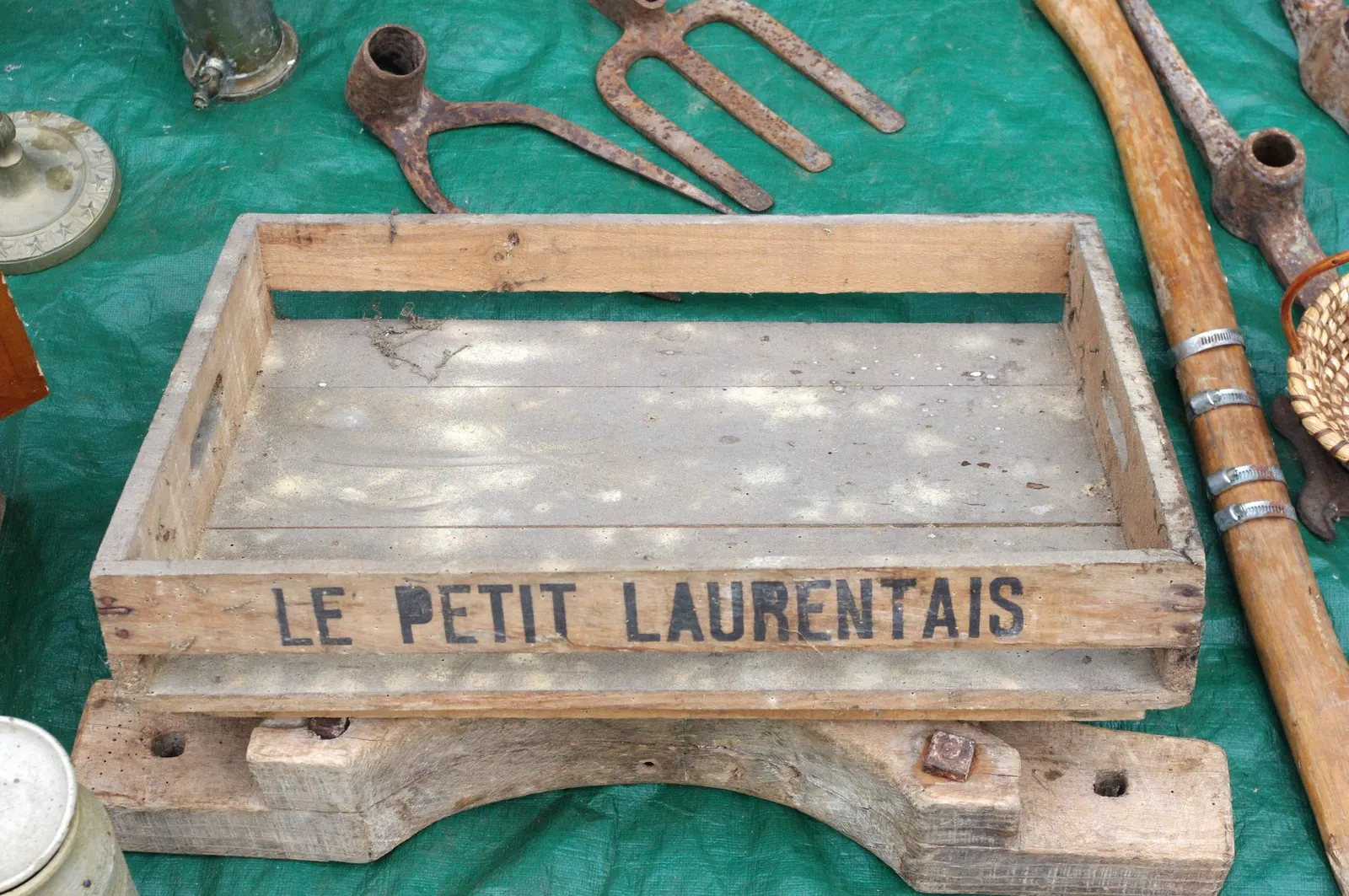 Caisse en bois, outils et ustensiles anciens posés sur une bâche verte de brocante