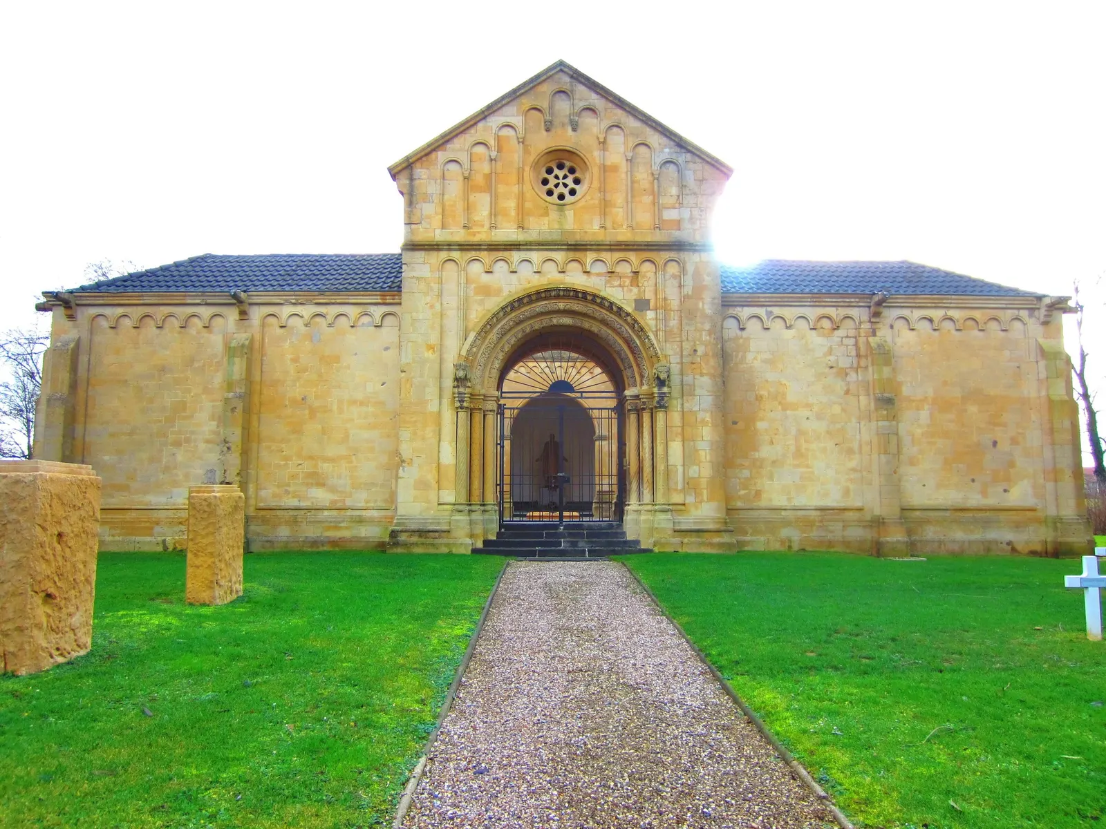 Façade en pierre jaune du mausolée du cimetière militaire de Gravelotte, au bout d'une allée de gravier bordée de pelouse