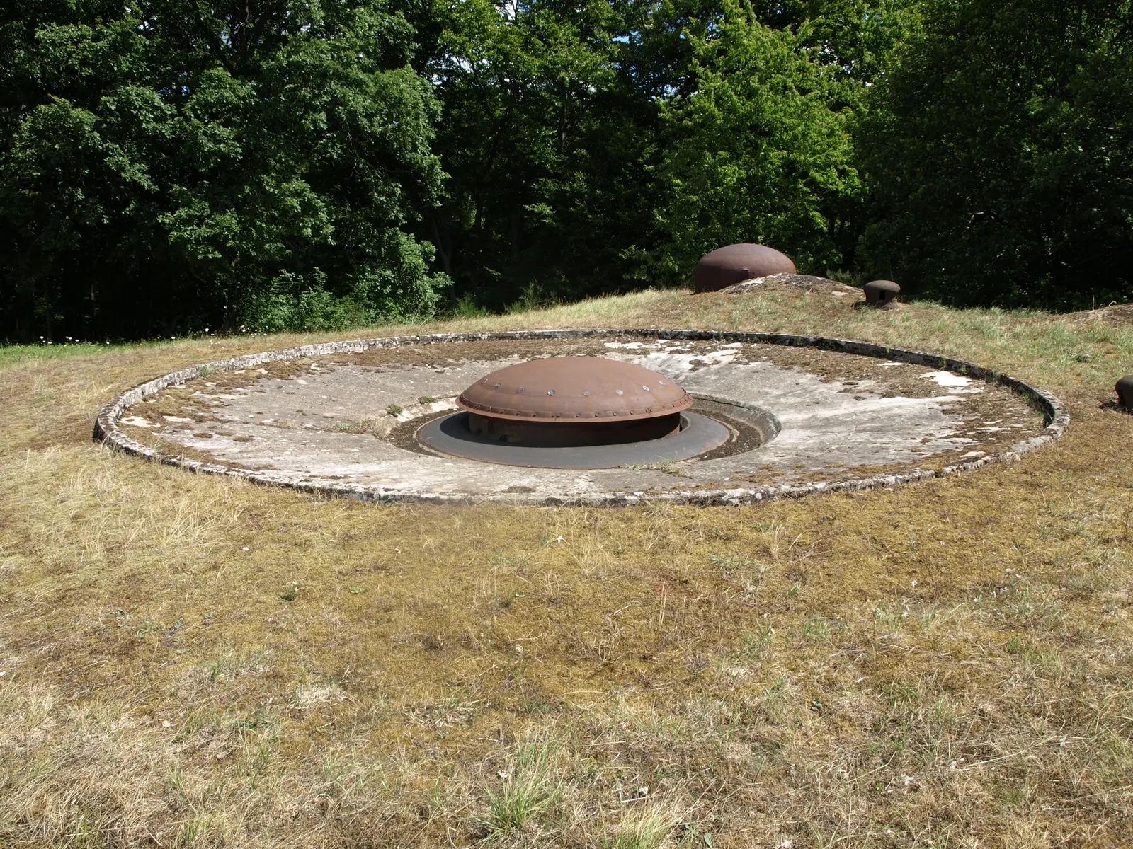 Tourelle d'artillerie en acier affleurant au milieu d'une dalle de béton, sur la colline herbeuse du Hackenberg