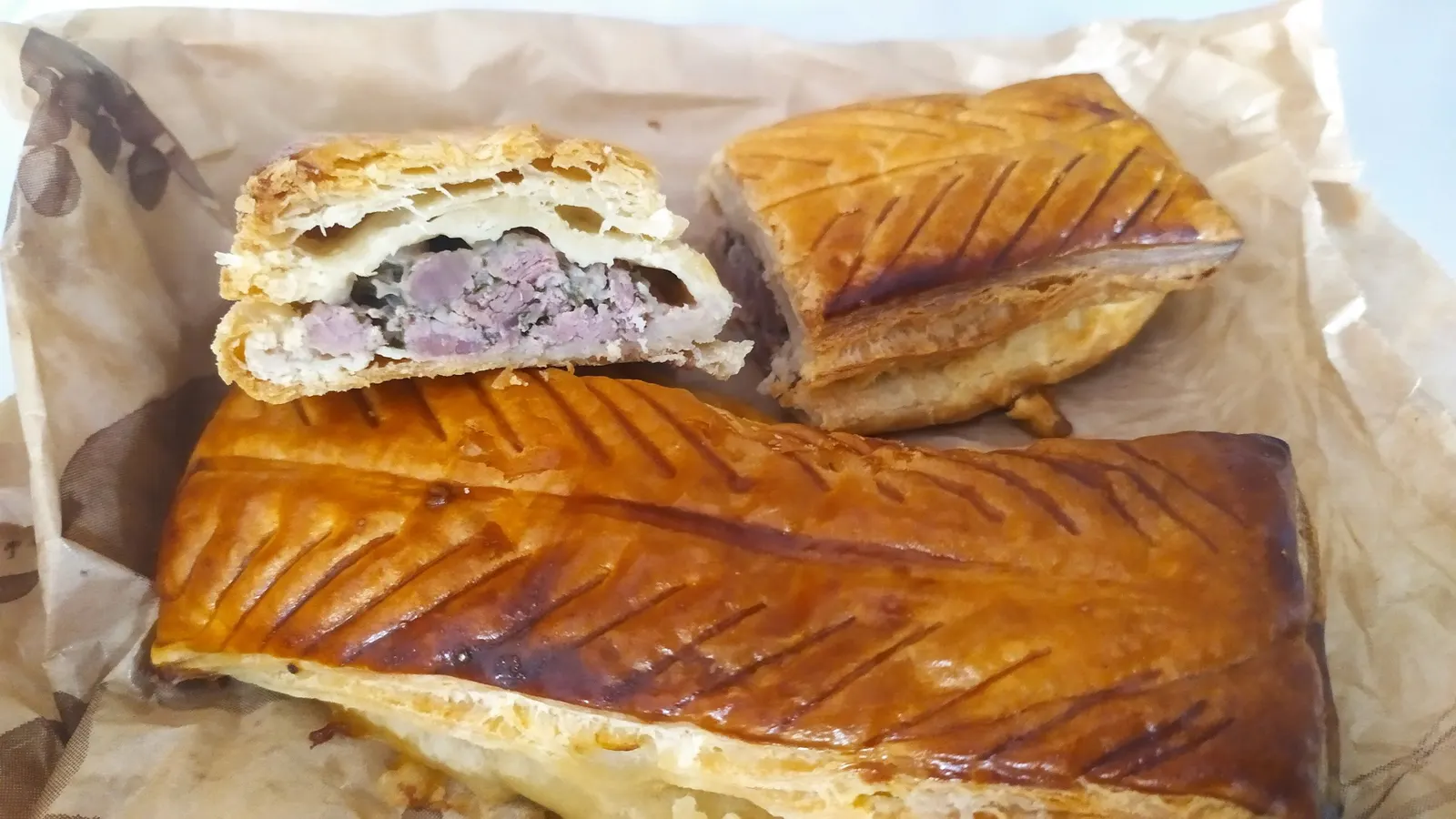 Pâtés lorrains dorés sur un papier, l'un coupé en deux montrant la farce de viande dans la pâte feuilletée